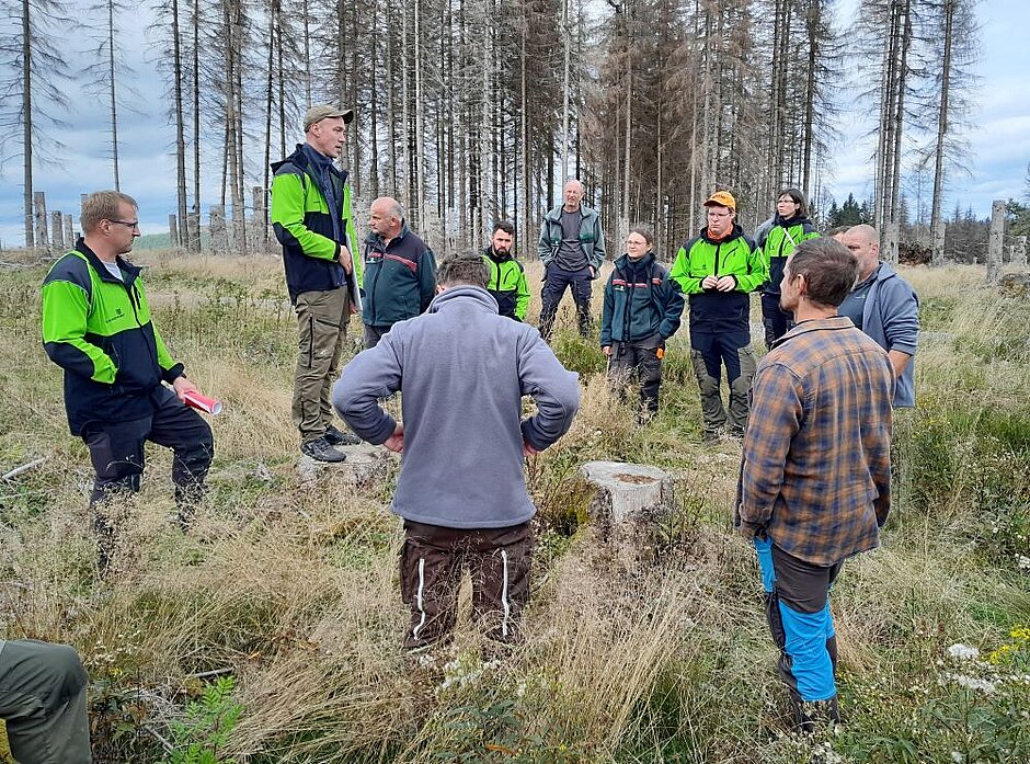 Revierleiter Jakob Strobel, Cursdorf/Forstamt Neuhaus stellt gerade an einem Exkursionspunkt das Waldbild vor. Die Teilnehmer stehen um ihn herum.